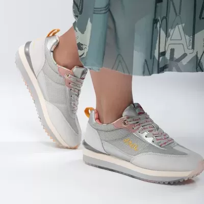 Sapatilhas cinzentas e rosa com sola branca usadas por pessoa com vestido azul claro com letras