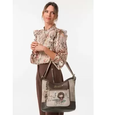 Mala de ombro bege e castanha da marca Anekke com ilustração frontal, em uso por mulher com blusa estampada e calças castanhas