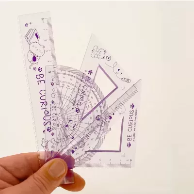 Conjunto de réguas transparentes roxas com desenhos de gatos e frases em inglês seguradas por uma mão.