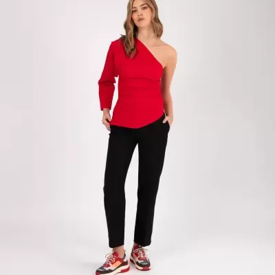Mulher com top vermelho de um ombro, calças pretas e ténis desportivos
