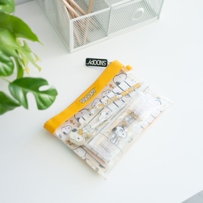 Estojo transparente com personagens Snoopy e fecho amarelo na mesa branca