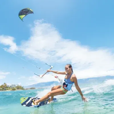 Mulher a praticar kitesurf no mar com prancha preta e céu azul