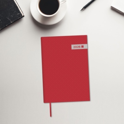 Agenda ou caderno vermelho com texto 2026 sobre mesa branca com café, caneta, caderno e bloco