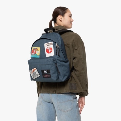 Mochila azul escura com patches coloridos usada por pessoa de casaco verde e jeans