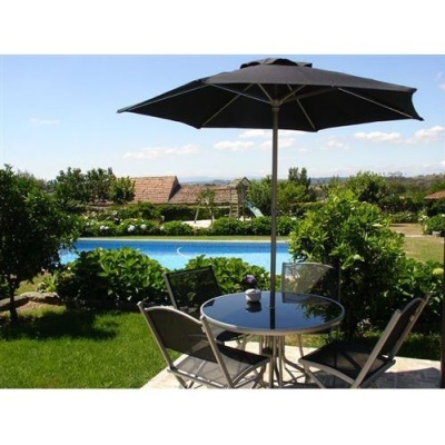 Conjunto de jardim com mesa redonda de vidro, quatro cadeiras metálicas pretas e guarda-sol preto junto a piscina