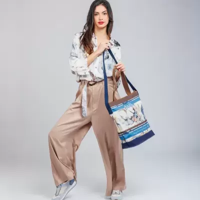 Mochila floral azul, bege e branco com texto L'AMORE transportada por mulher com calças taupe e camisa branca