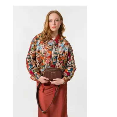 Mulher a usar blazer colorido floral e saia coral, segurando mala castanha Anekke