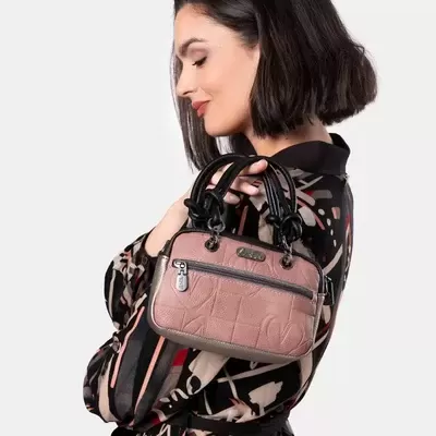 Mala de mão rosa com detalhes pretos e fecho frontal, segurada por mulher num vestido estampado.