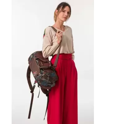 Mochila castanha com padrão patchwork usada por mulher com camisola bege e calças vermelhas