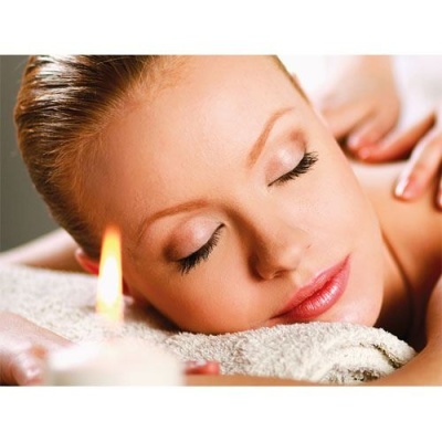 Mulher relaxando em spa com toalha branca e vela acesa