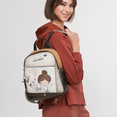 Mochila pequena ilustrada bege e castanha com texto, usada por mulher com roupa castanha.