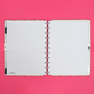 Caderno de argolas aberto com uma página pautada e outra em branco sobre fundo rosa