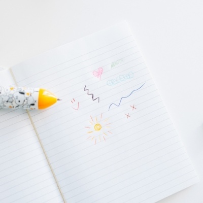 Caneta decorada amarela sobre caderno com desenhos coloridos