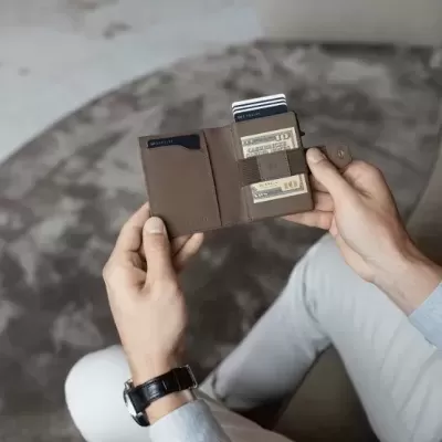 Carteira de couro castanha aberta com cartões à mão de pessoa sentada em ambiente interno