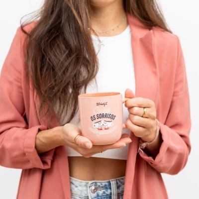Caneca cor-de-rosa com texto em português segurada por mulher com casaco cor-de-rosa