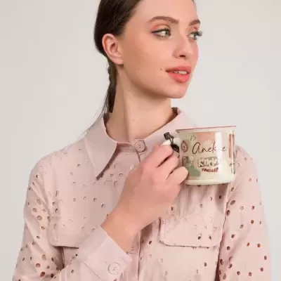 Mulher segurando caneca com design e texto, vestindo camisa rosa com padrão recortado
