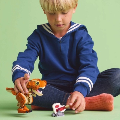 Menino a brincar com brinquedo de montar dinossauro laranja e branco.