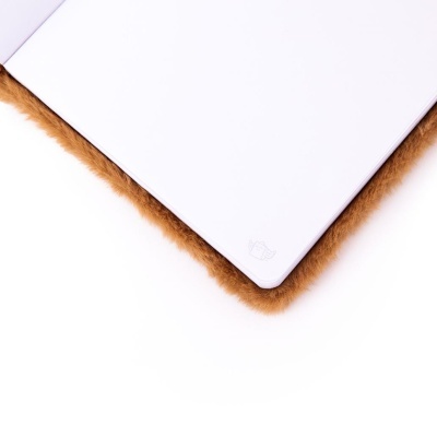 Caderno branco com logotipo de livro com asas sobre superfície felpuda castanha