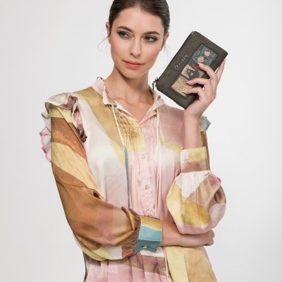 Carteira castanho escuro com estampas coloridas nas mãos de mulher com camisa estampada em tons pastel