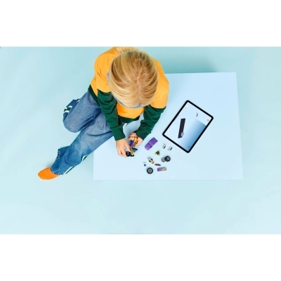 Criança a montar brinquedo de construção com peças coloridas e tablet com instruções em mesa branca