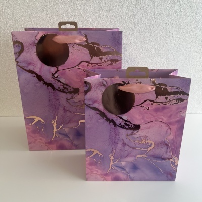 Sacos de presente em padrão abstrato roxo com alças embutidas sobre mesa branca