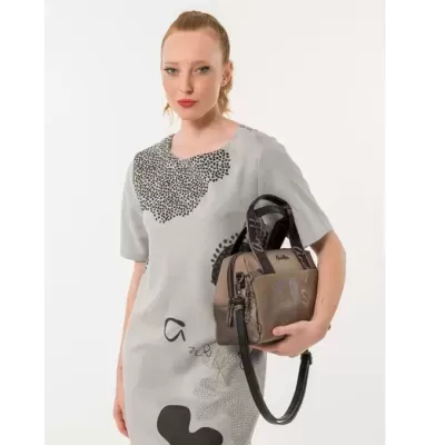 Mulher com vestido cinza claro segurando mala castanha