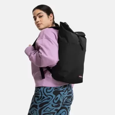 Mochila preta Eastpak com aba e fivela usada por mulher com sweatshirt lavanda e calças com padrão abstrato azul e preto
