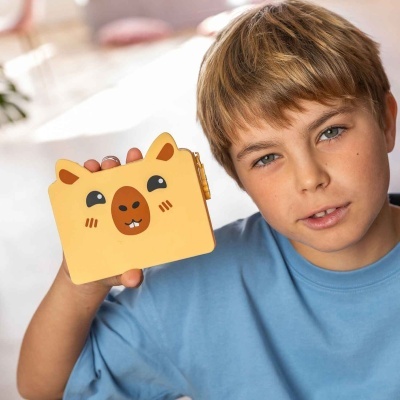 Menino com carteira amarela em silicone com rosto de animal sorridente.