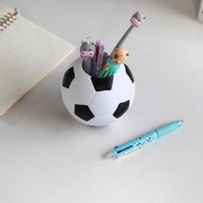 Porta canetas bola de futebol com canetas coloridas e personagens de animais numa mesa branca.