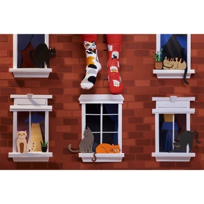 Meias com padrão de gatos coloridas penduradas na frente de uma parede de tijolos com janelas ilustradas com gatos.