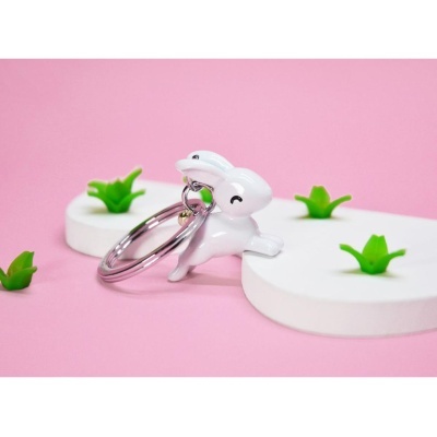 Chaveiro coelho branco sorridente sobre base branca com detalhes verdes e fundo rosa