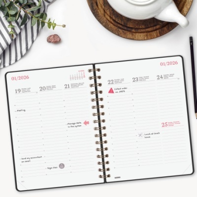 Agenda semanal aberta com caneta, ramo verde, pano riscado, pedra e bule branco sobre prato de madeira