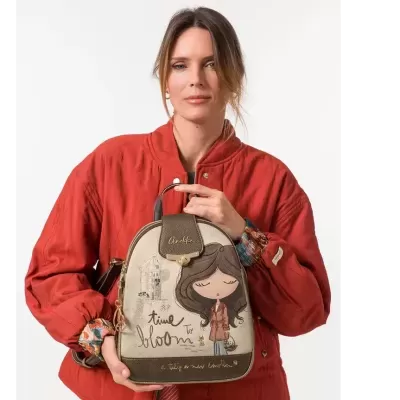 Mochila bege e castanha com desenho de personagem feminina e texto, segurada por mulher de casaco vermelho.