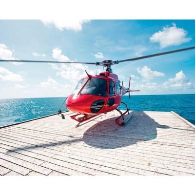 Helicóptero vermelho numa plataforma de madeira à beira-mar sob céu azul