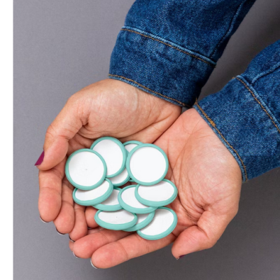 Mãos segurando fichas redondas verde e branco sobre fundo cinzento