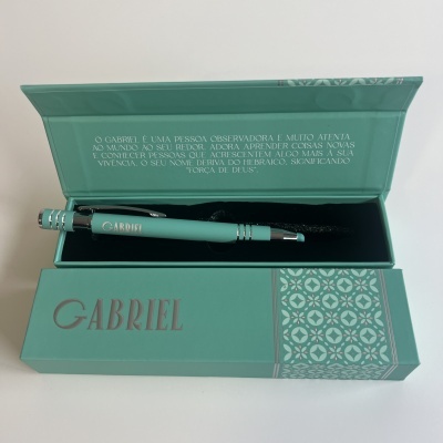 Caneta verde-água em estojo verde-água com padrão geométrico e texto interno