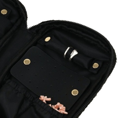 Estojo preto aberto com anel prateado, colares com contas cor de rosa e painel preto com botões dourados