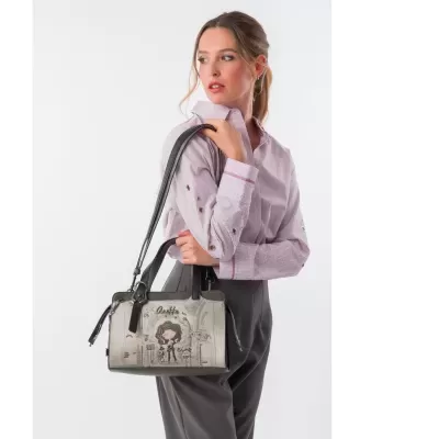 Mala bege e cinzenta com desenhos e texto, segura por mulher com camisa rosa clara e calças cinzentas.