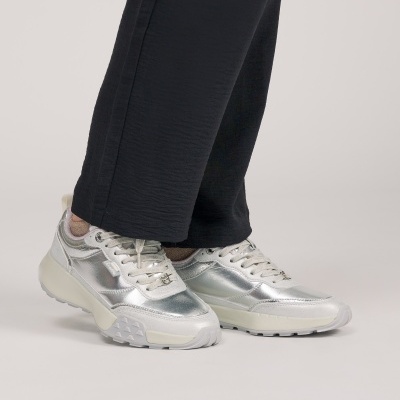 Ténis prateados metálicos usados com calças pretas.