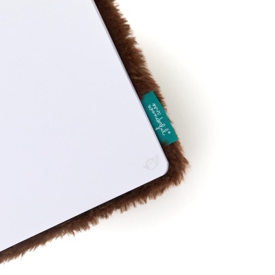 Caderno branco com canto arredondado sobre superfície castanha peluda com etiqueta azul mr. wonderful.