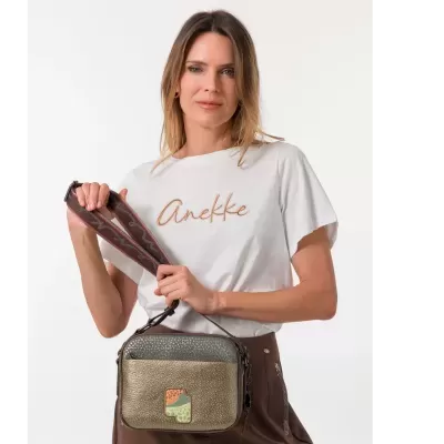 Mulher com t-shirt branca segurando mala de ombro texturizada em dourado e castanho