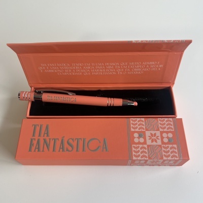 Conjunto caneta e caixa coral com texto TIA FANTÁSTICA e padrão geométrico.