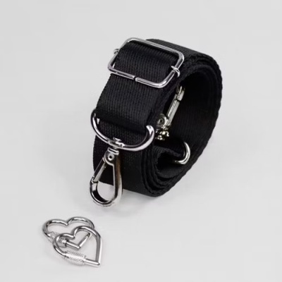 Alça preta de tecido com ferragens metálicas prateadas e dois mosquetões em forma de coração no fundo branco.