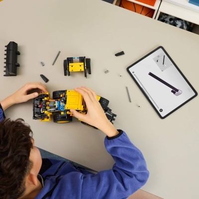 Criança a montar veículo de construção Lego amarelo e preto com tablet a mostrar instruções.