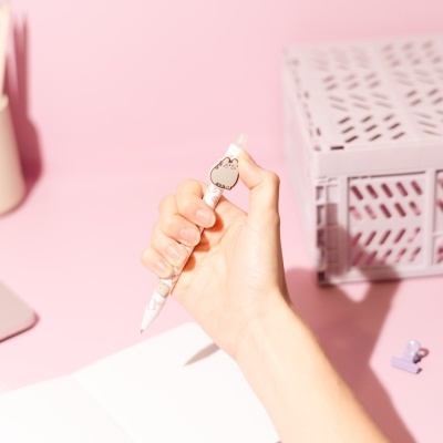 Caneta branca com desenhos de gatos cinzentos numa mesa cor-de-rosa