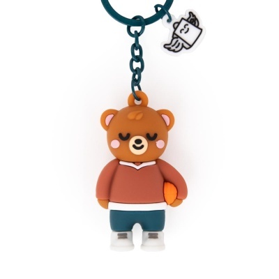 Chaveiro emborrachado de urso castanho vestido com roupa casual segurando bola laranja.