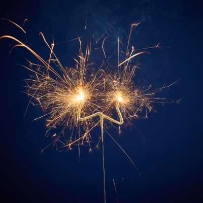 Dois desenhos de fogo de artifício acesos em suporte metálico contra fundo azul escuro