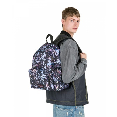 Mochila Eastpak colorida com padrão abstrato usada por um jovem com casaco cinzento e jeans azuis.