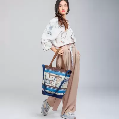 Mulher com camisa branca estampada, calças bege e mala tote azul com estampado colorido