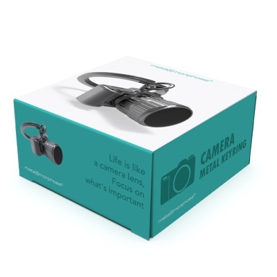Porta-chaves metálico em forma de lente de câmera com embalagem azul e branca